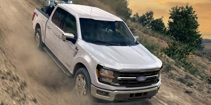 A white Ford F-150 truck driving off-road, kicking up dust.