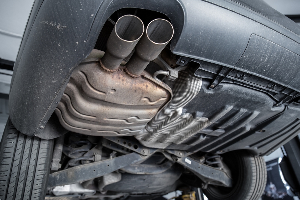A close-up view of a car's exhaust system, showing the muffler and dual exhaust pipes from underneath the vehicle.