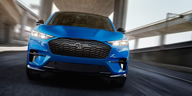 Front view of blue Ford Mustang Mach-E driving under overpass