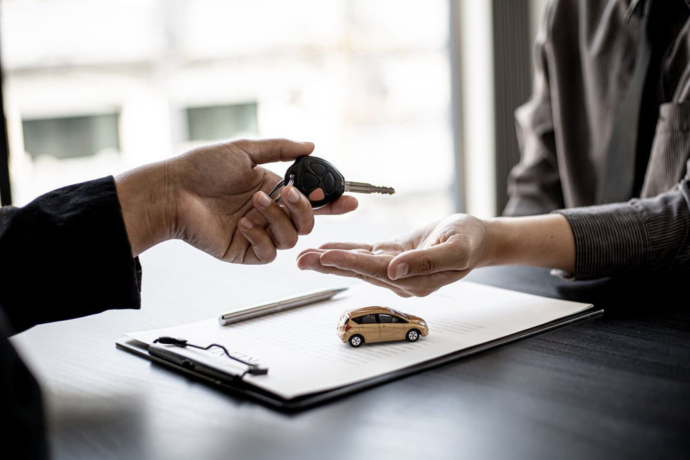 A man hands a car key to a woman, symbolizing the transfer of ownership or financing of a vehicle.